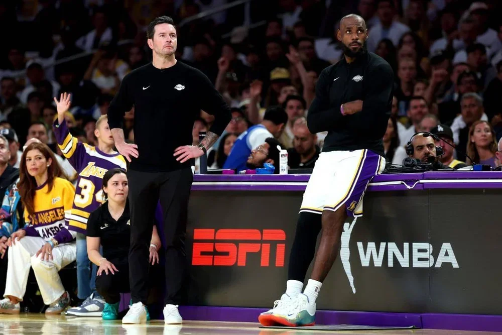 JJ Redick and LeBron James look on from the sideline in Game 3 against the Thunder. Redick stands with his hands on his hips, and James leans against the scorer's table with his arms crossed, both wearing grim expressions.